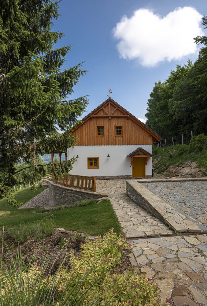 Dřevo, kámen a bílá barva fasády dávají domu jednoduchý horský styl, stavba do okolní přírody dobře zapadá
