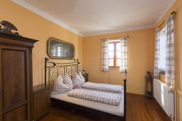 V této ložnici je kovová postel a stěny mají příjemnou meruňkovou barvu